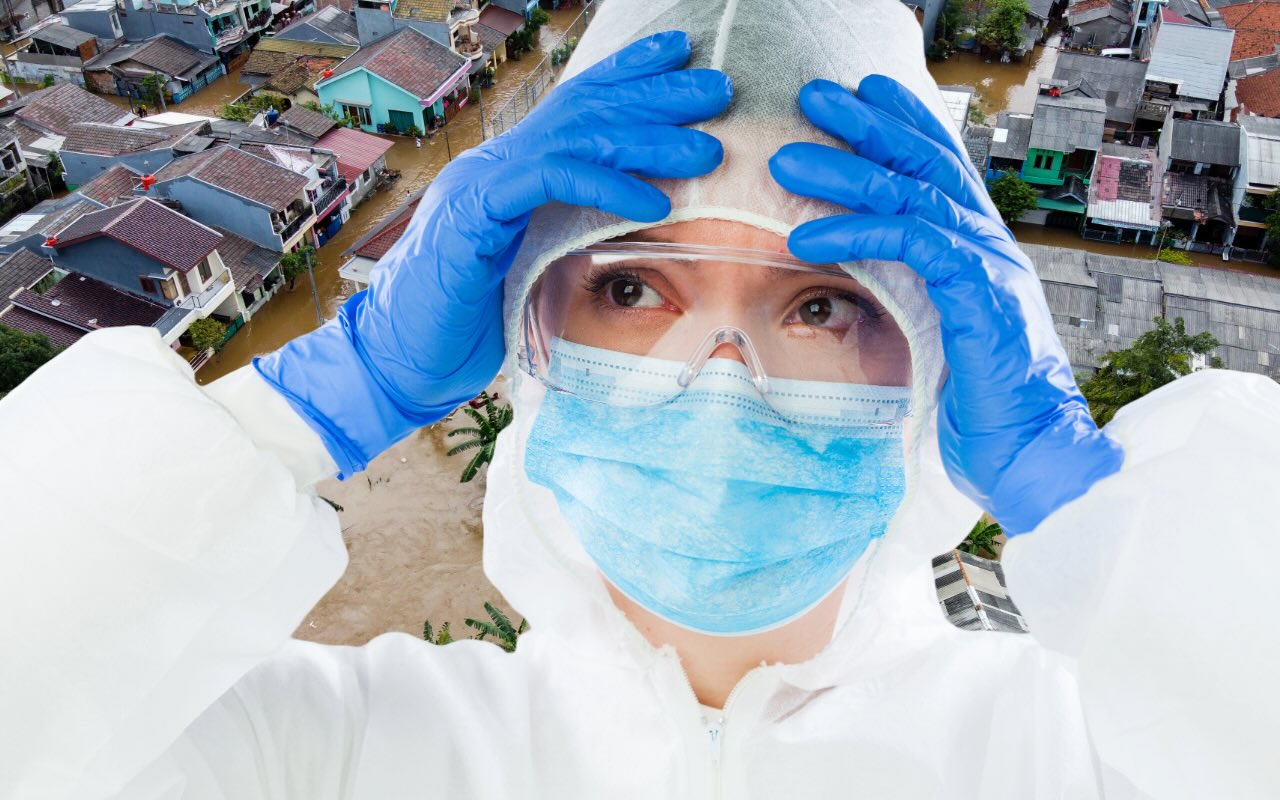 woman in white coveralls and mask - ppe - in front of disaster flooded town